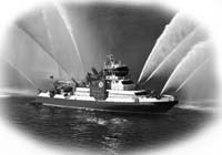 Fire boat pumping out giant streams of water to extinguish a fire at sea.