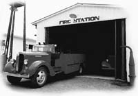 Black and white image of a small two truck fire station in Chile with a vintage fire truck parked in front